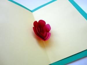 Tarjeta blanca abierta con una rosa de papel en el centro 